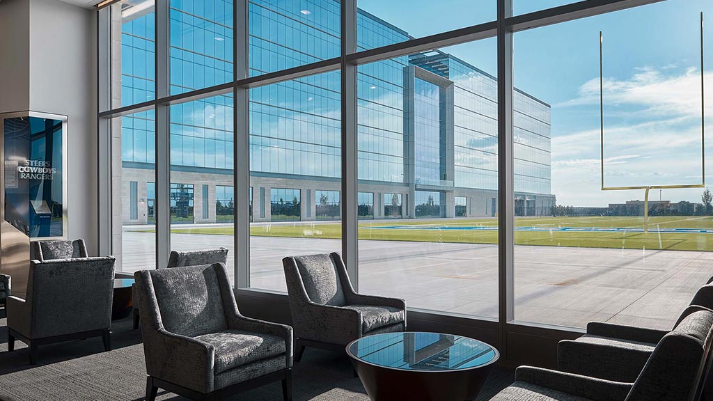 A room with a large window and a large glass wall with a large courtyard and a large green.