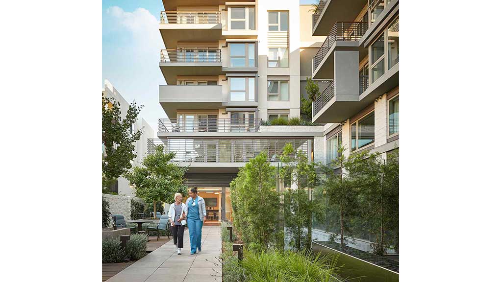 A couple of people walking on a sidewalk next to a building.