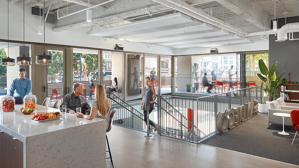 A group of people in a large room with tables and chairs.