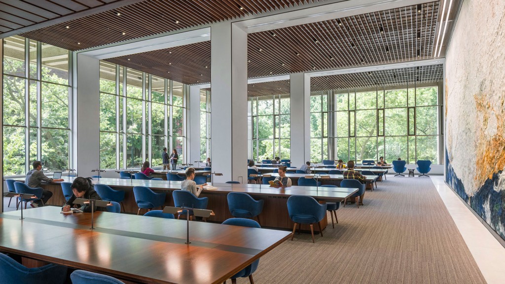 A group of people sitting at tables in a large room with large windows.