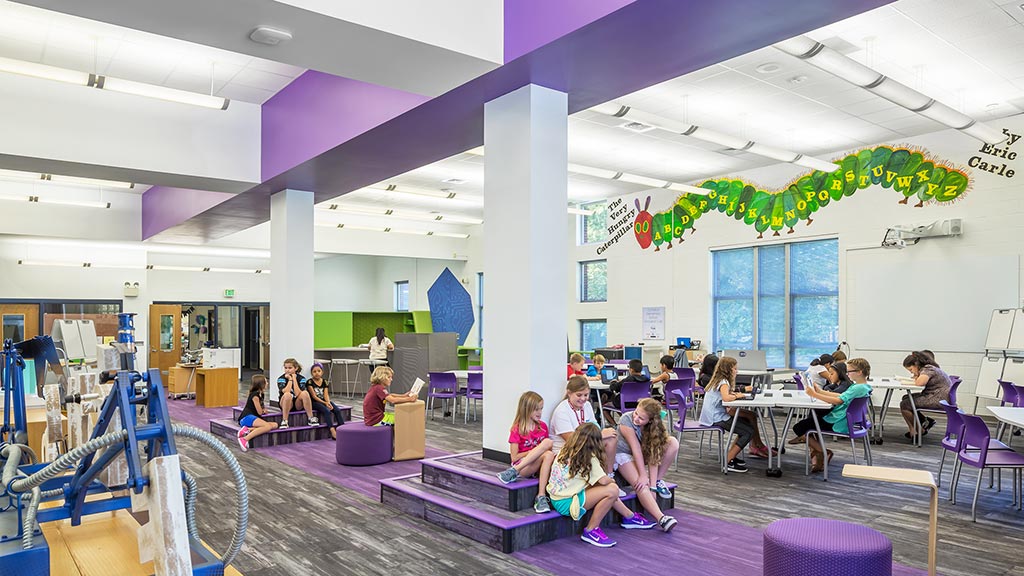 A group of people sitting on purple chairs in a room with a stage.