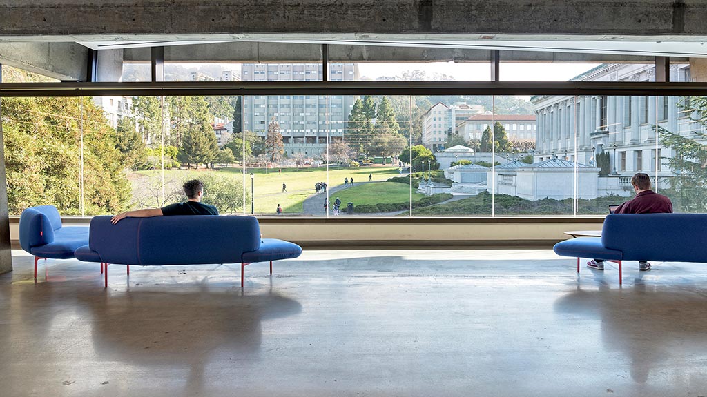 A couple of people sitting on a bench in a large room with a large window.
