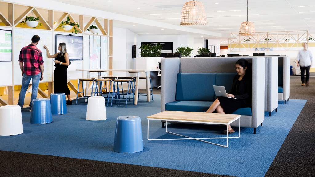 A person sitting on a couch with a laptop in a room with people.