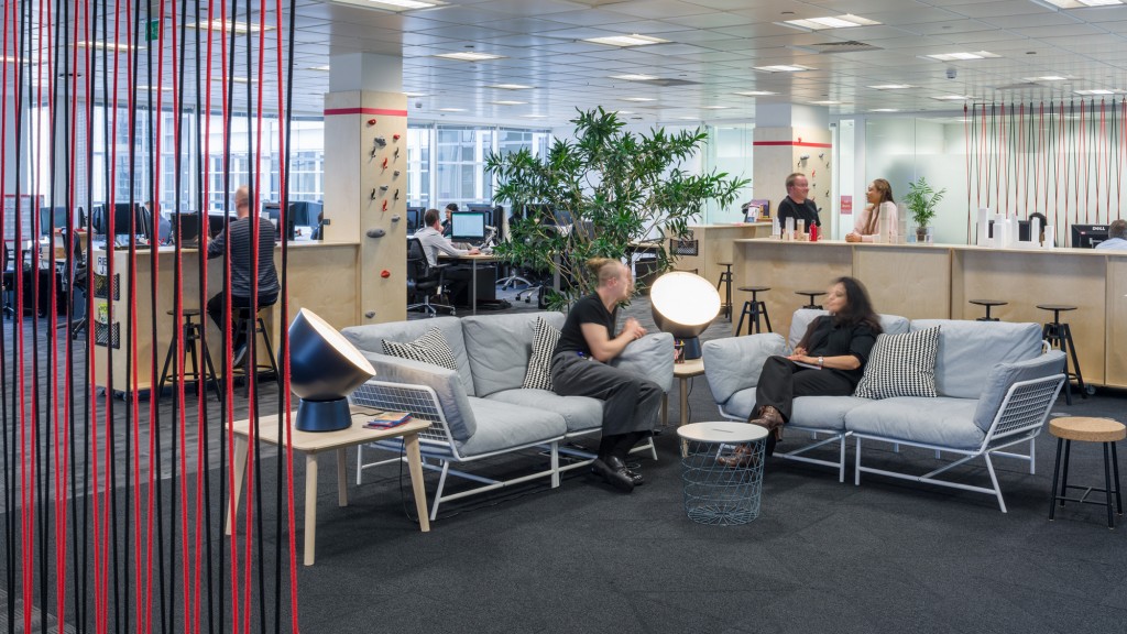 A group of people sitting on couches in a room with a glass wall and a tree.