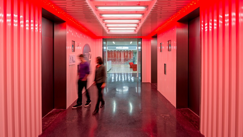 A couple of people walking through a hallway with red walls.