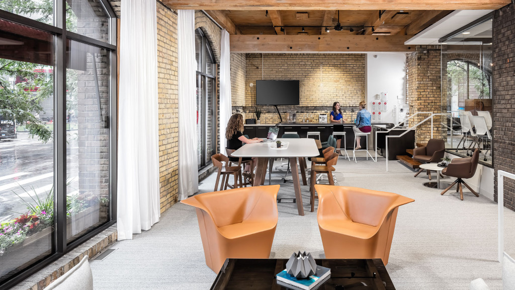 A group of people sitting at a table in a room with a brick wall and windows.