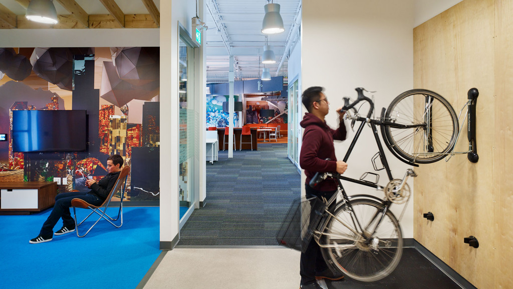 A person holding a bicycle in a room with a person sitting in a chair.