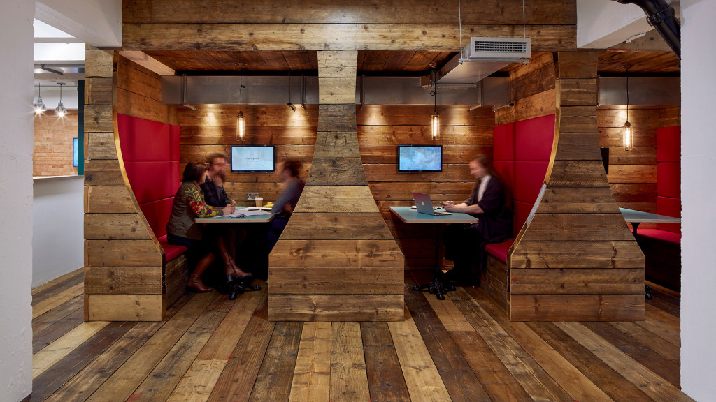 A group of people sitting at a table in a room with a red wall and wood floor.