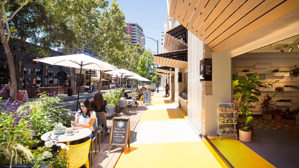 A group of people sitting at tables outside a building.