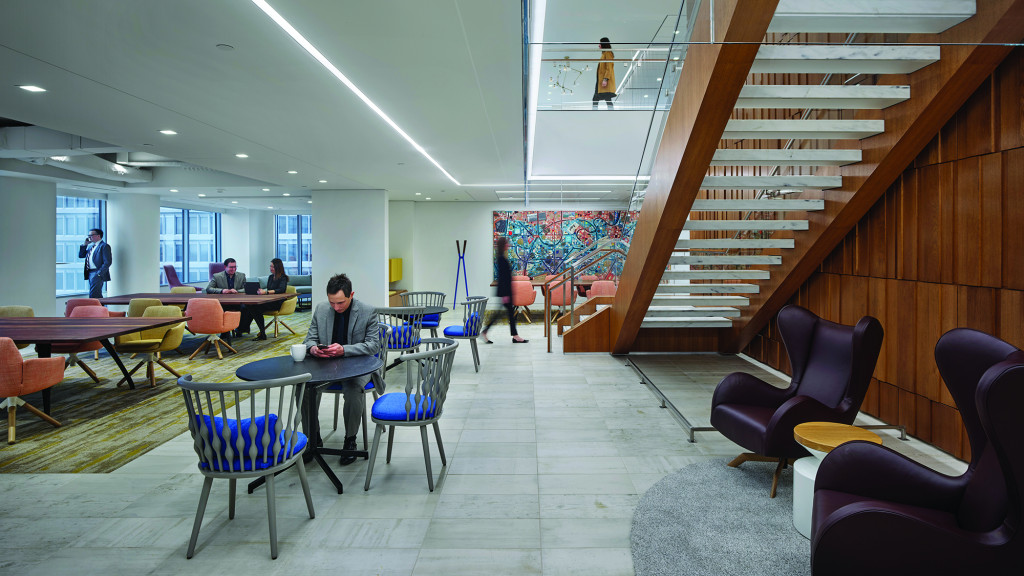 A group of people sitting at tables in a room with stairs.