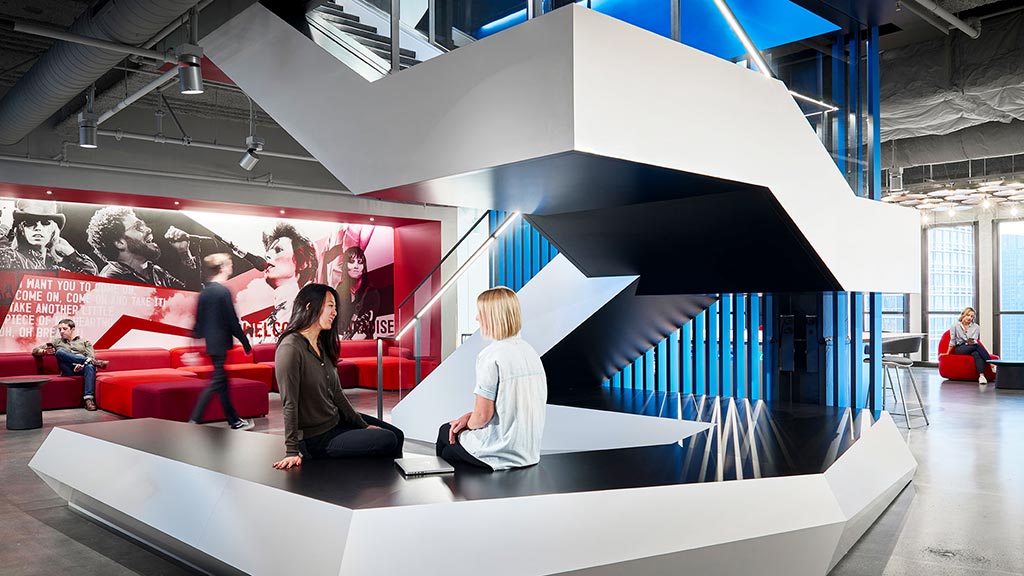 A group of people sitting on a white table in a room with a large screen.
