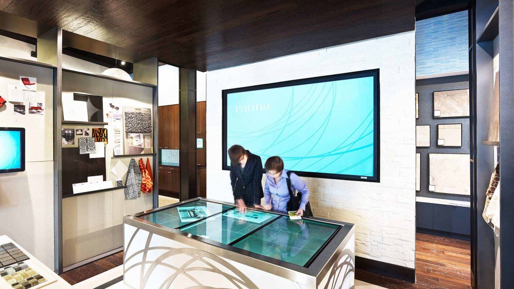 A couple of men sitting at a table in front of a large screen.