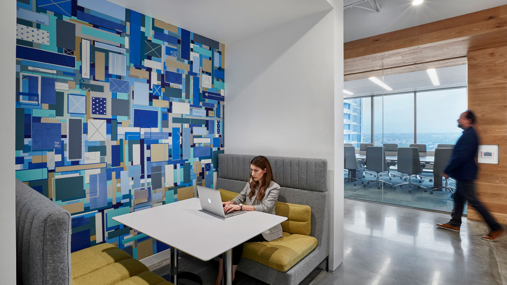 A woman sitting on a couch with a laptop in a room with a man standing and a woman.