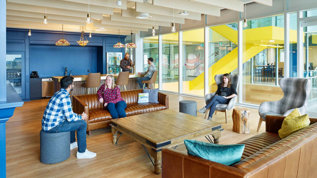A group of people sitting on couches in a room with a glass wall and a table.