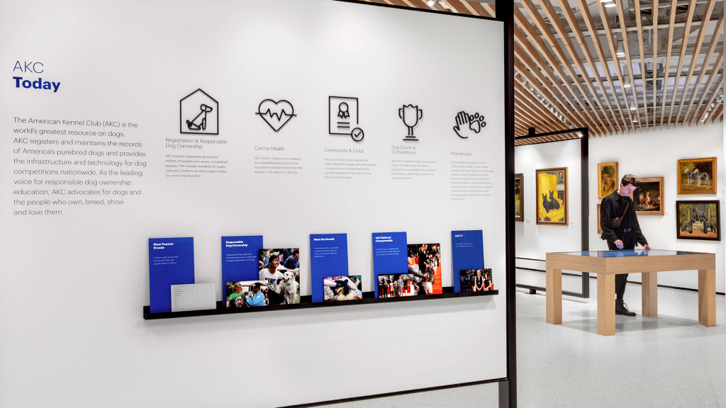 A person standing in a room with a table and a wall of pictures.