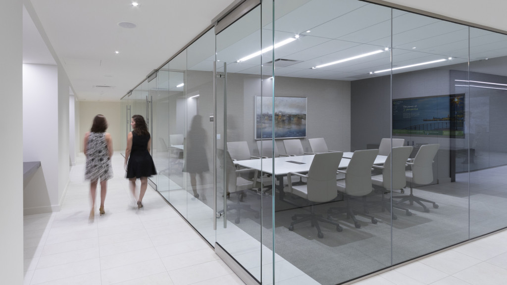 A couple of women walking in a room with white chairs and a table.