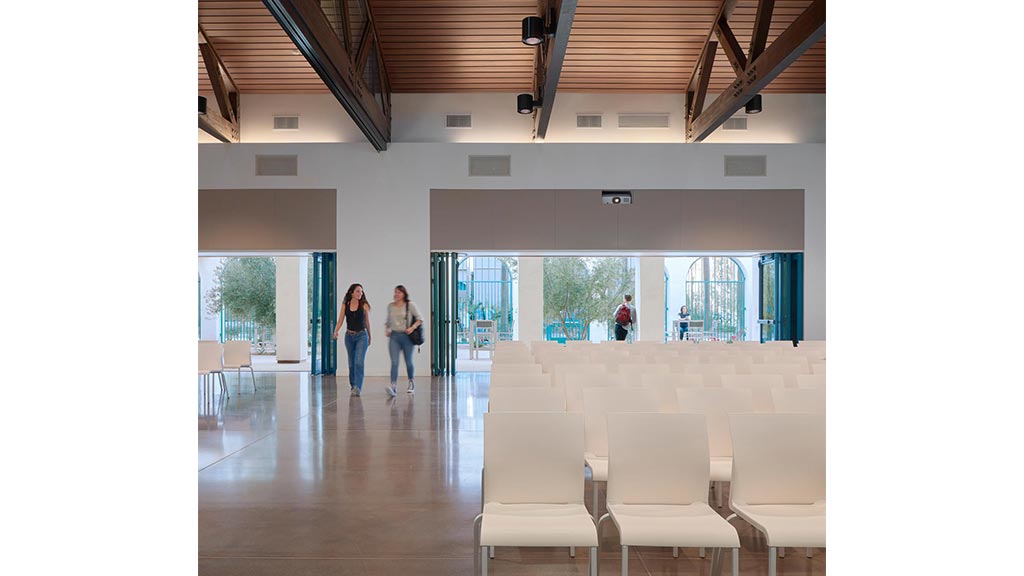A couple of women walking in a large room with white chairs.