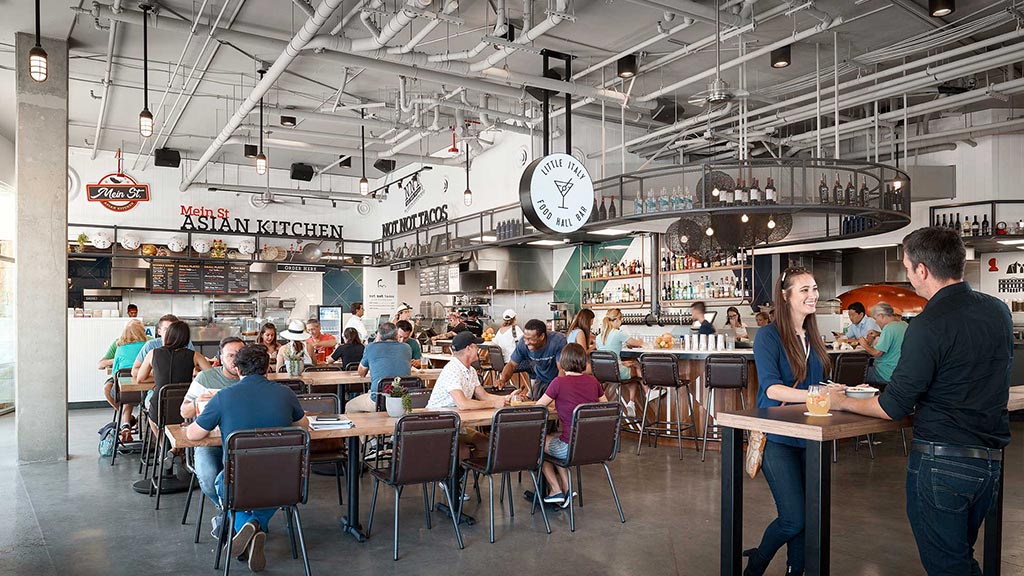 People sitting at tables in a large room with a clock.