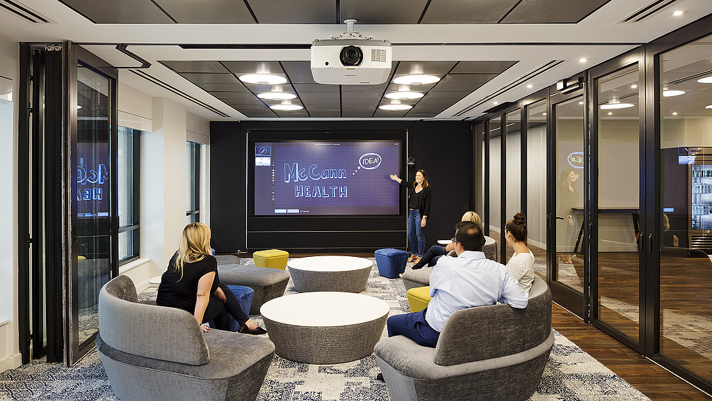 A group of people sitting in a room with a large screen.