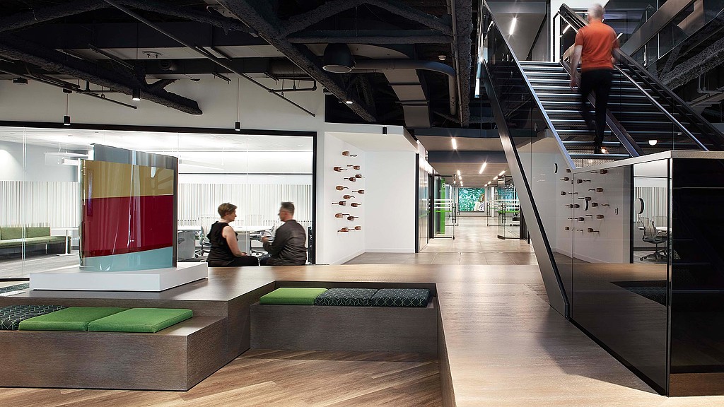 A person standing on a podium in a room with a person sitting on a bench.