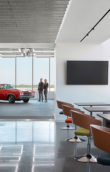 A couple of people standing in a room with chairs and a table.