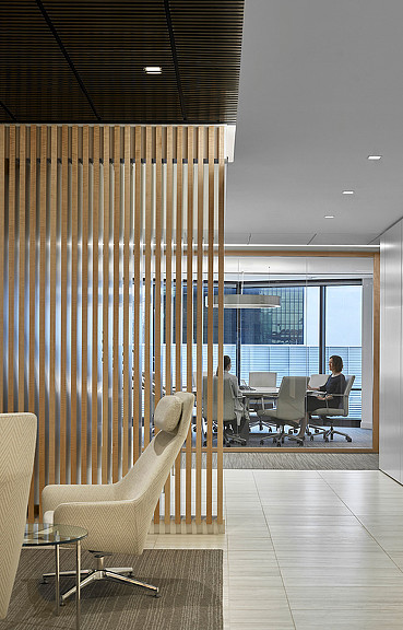 A room with a glass wall and a table with chairs and a person sitting at a desk with.