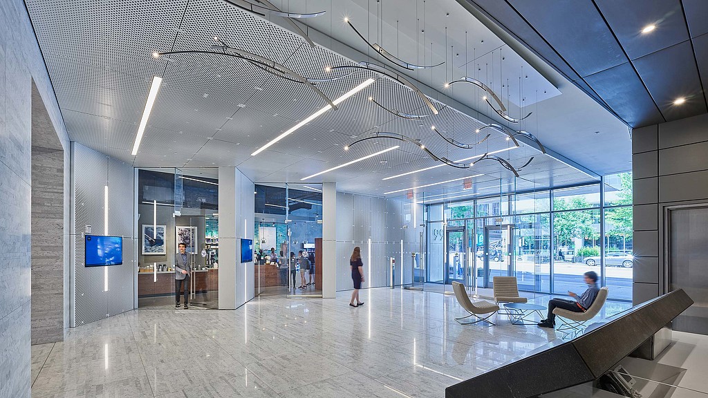 A large glass walled building with people and a person sitting on a bench.