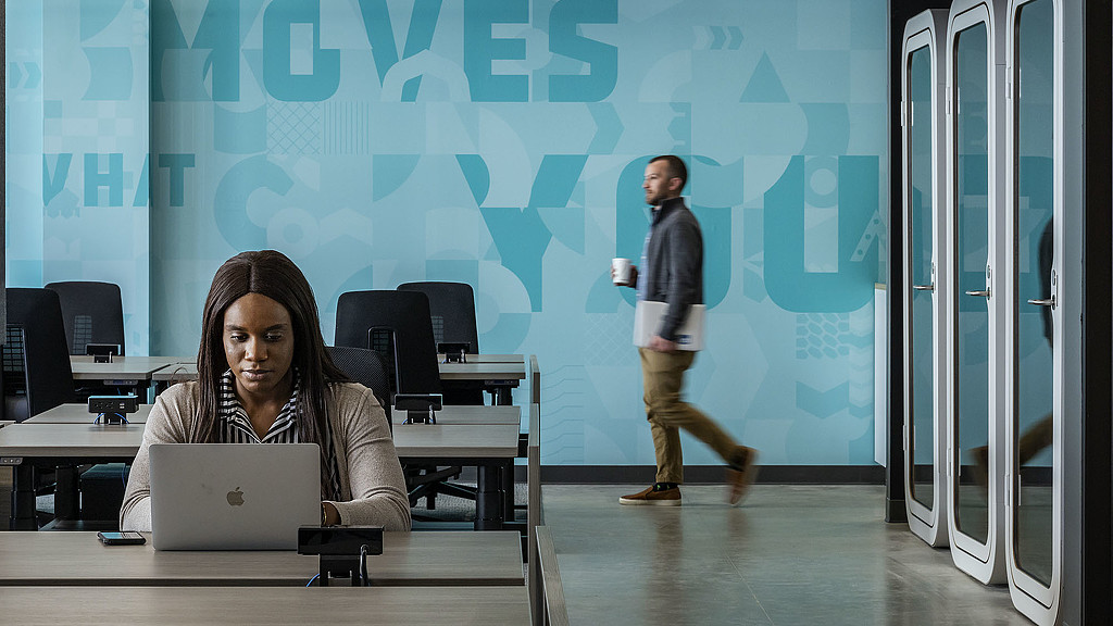 A woman sitting at a desk with a laptop in front of a man.