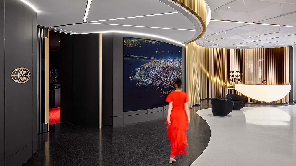 A person in an orange dress walking in a room with a large screen.