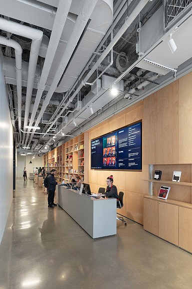 A person sitting at a desk in a large room with a large screen.