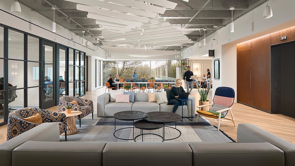 A person sitting on a couch in a large room with a large glass wall and a table with.