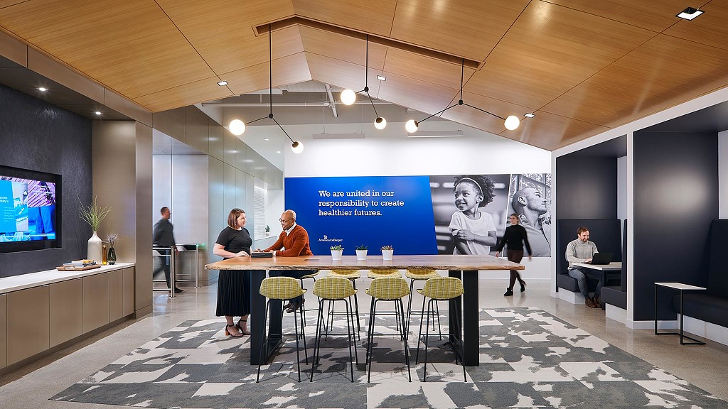 A group of people sitting at a table with a large screen behind them.