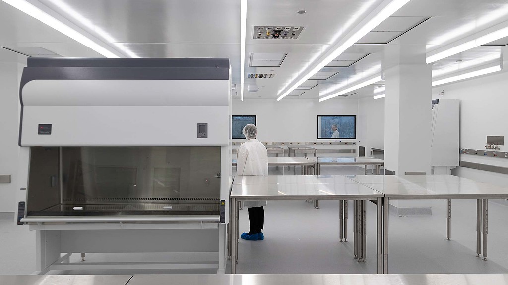 A person in a white coat in a room with a large glass table.