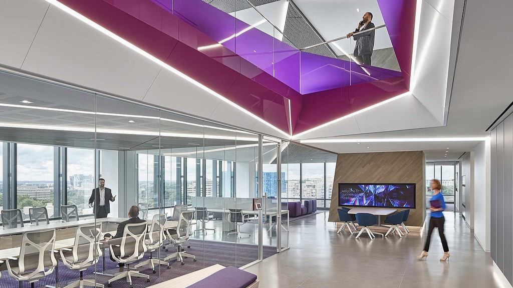 A room with a large screen and chairs and people walking around.