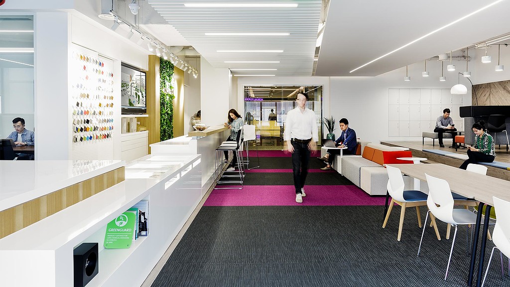 A person walking in a room with people sitting at tables and chairs.