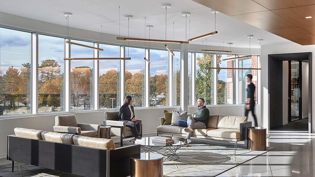A man and woman sitting on a couch in a large room with large windows.