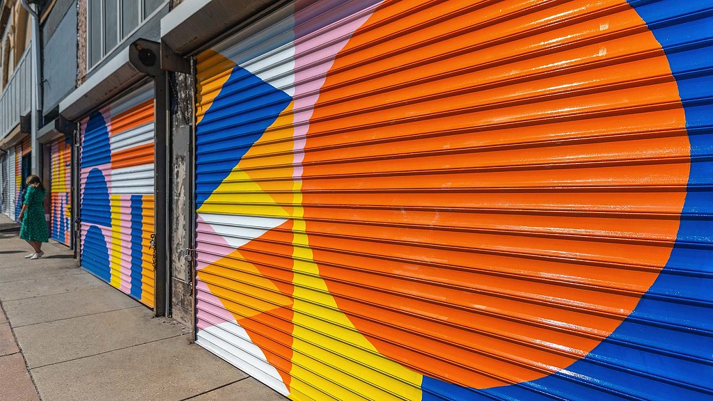 A person walking on a sidewalk next to a wall with colorful paintings.