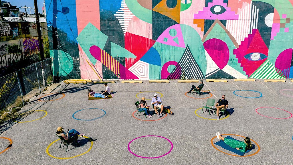 A group of people sitting on a bench in front of a wall with graffiti.