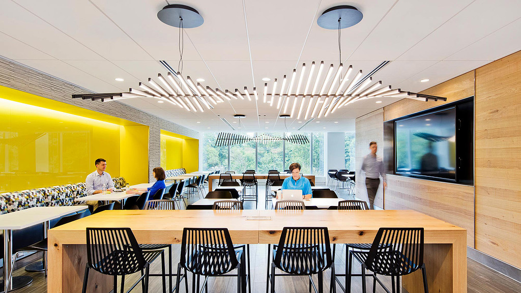 A group of people sitting at tables in a room with a large screen.