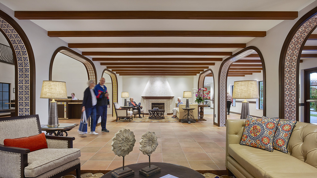 A couple of people walking in a large room with a fireplace.