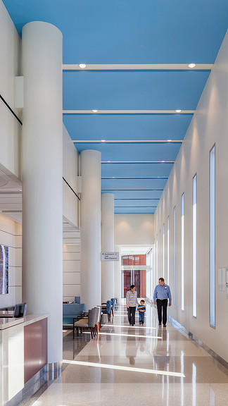 A person and a child walking in a large room with white pillars.