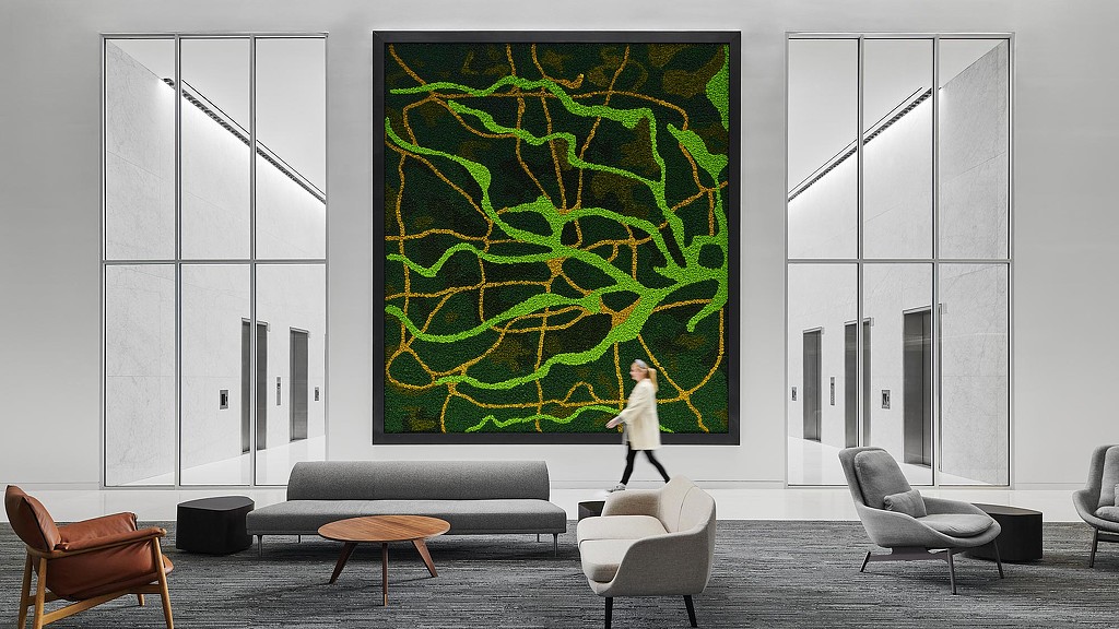 A person walking in a room with a large green screen.