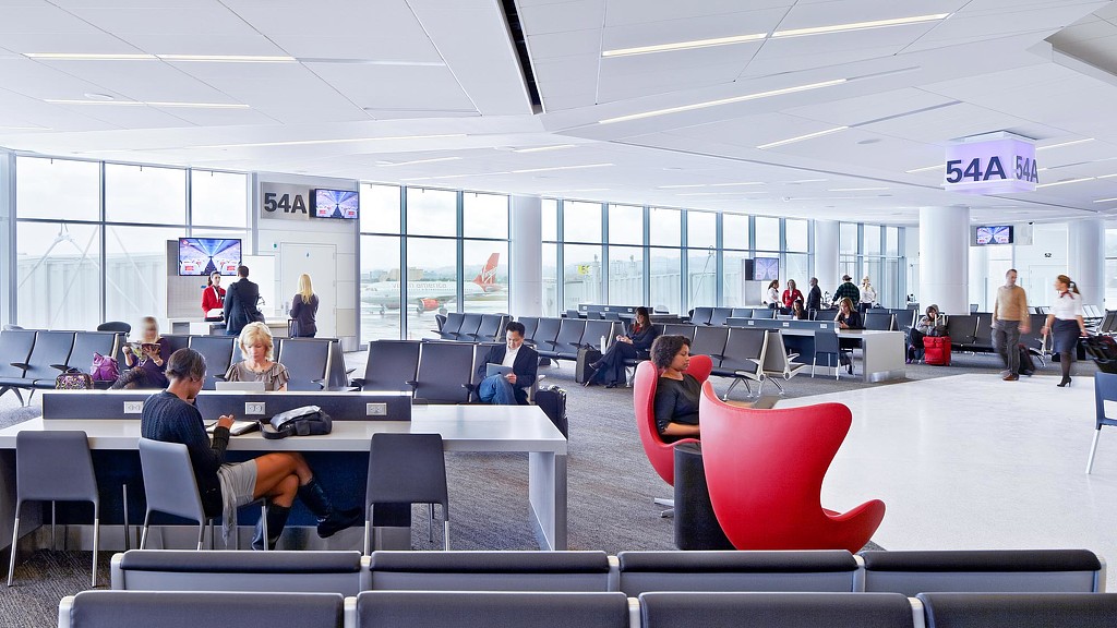 A group of people sitting at tables in a large room with windows.