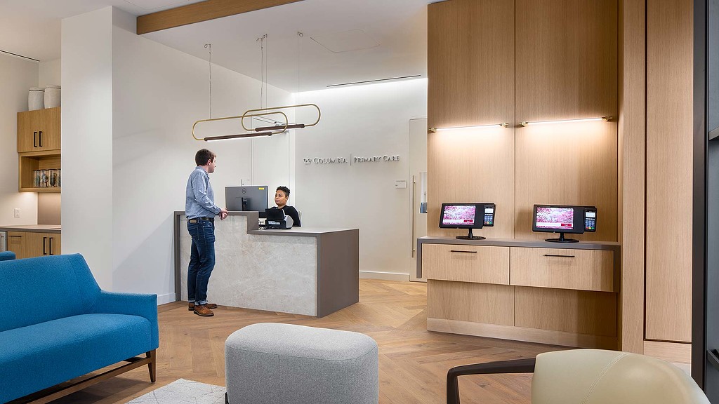 A person standing in front of a person sitting at a desk.