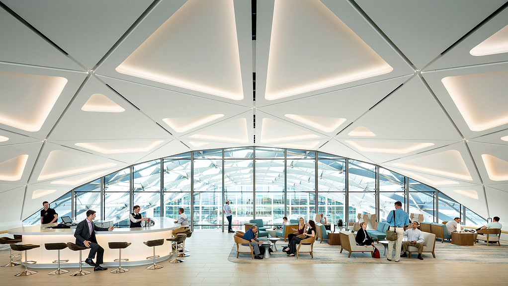 A group of people sitting in a large room with windows.