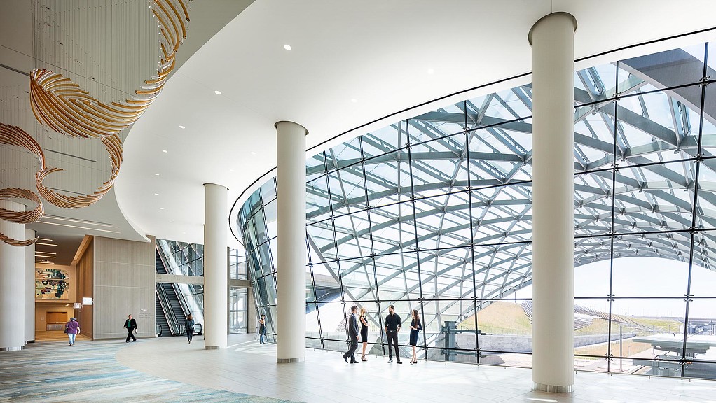 A group of people walking inside a building with glass walls.