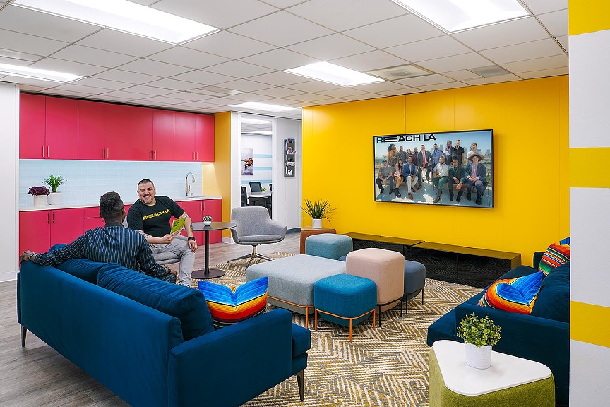 A couple of men sitting in a room with blue couches.