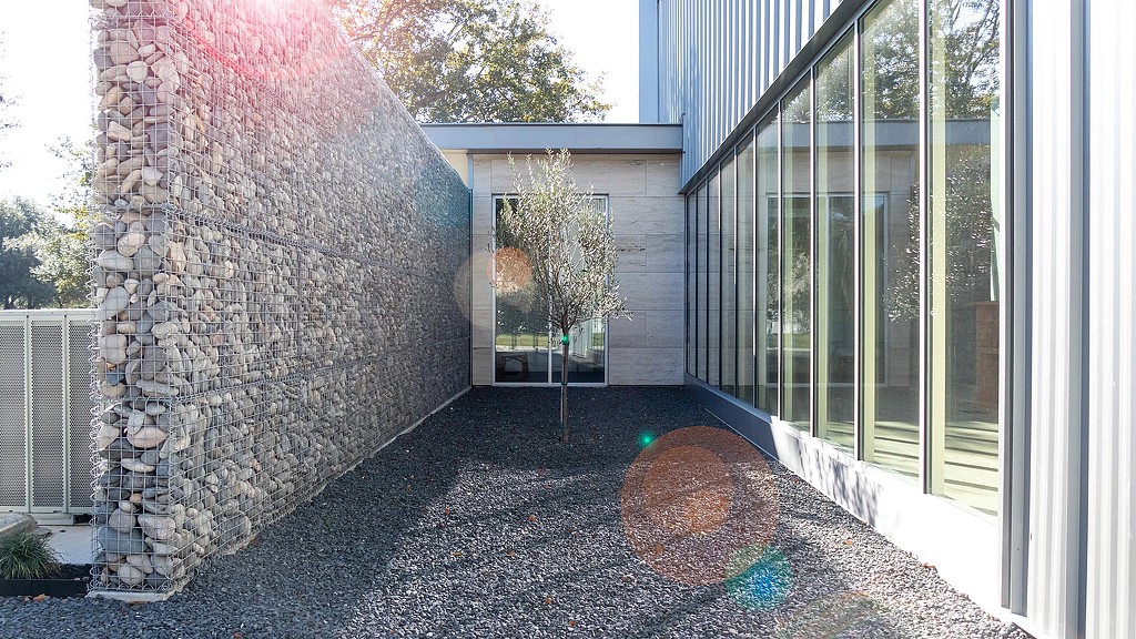 A stone wall with a tree and a building in the background.