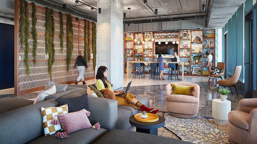 A couple of women sitting on a couch in a room with a bar and a person standing in.
