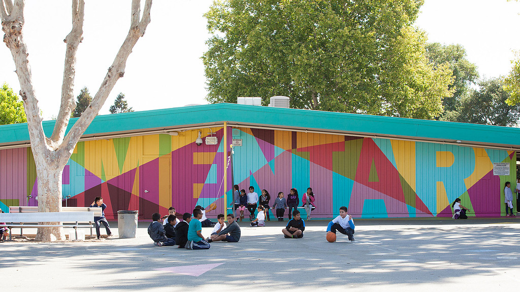 A group of people sitting on the ground in front of a colorful wall.
